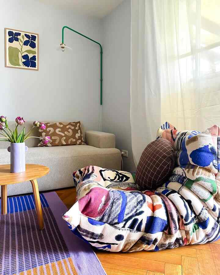 Bright natural color living room with beige sofa, colorful bean bag, wooden side table, and sheer curtains creating a cozy ambiance