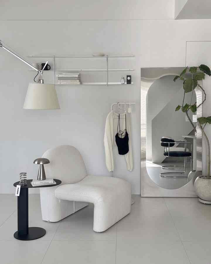 白とシルバーのトーンが特徴のリビング、シンプルなアームチェアとサイドテーブル、大型の全身鏡が配置されたモダンでミニマルな空間