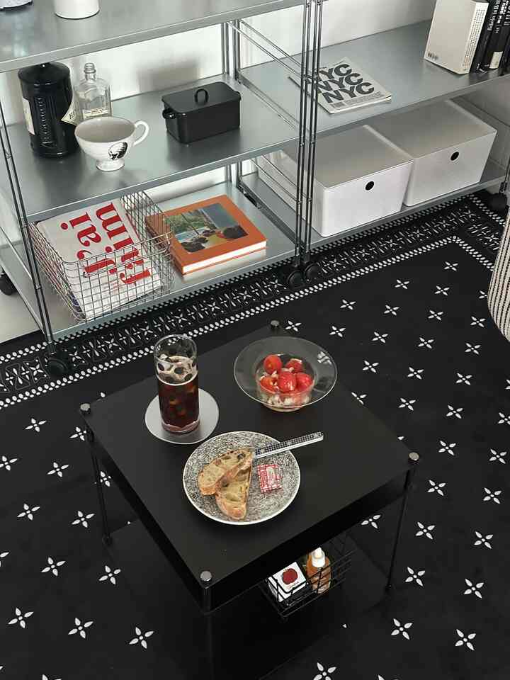 ブラックパターンのラグと中央に黒いコーヒーテーブル、透明なガラス皿と飲み物が置かれた洗練されたリビング