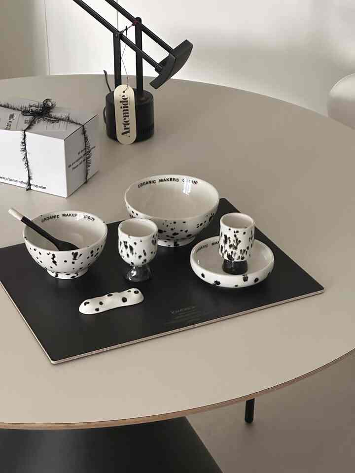 ベージュの丸テーブルの上に黒いランチョンマットと白地に黒のスポット模様の陶器が配置されたモダンなダイニングスペース