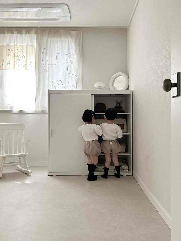 明るくナチュラルな色調の子供部屋、白いクローゼットとカーテン、二人の子供が立つシンプルな空間