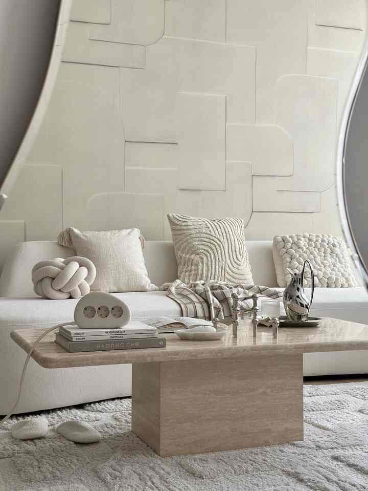 ベージュとホワイトのトーンが特徴のリビング、幅広いテクスチャのクッションと大理石のコーヒーテーブルが調和する居心地の良い空間