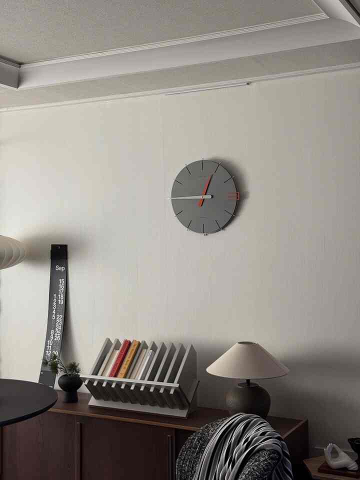 白い壁と木目調の収納家具があるシンプルでモダンなリビング、壁時計と本棚が配置された雰囲気のあるインテリア