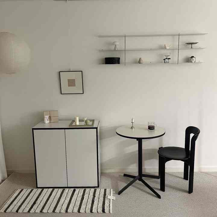 Minimal home cafe space in white and black tones featuring a round 600 table, chair, and wall shelf with a clean atmosphere