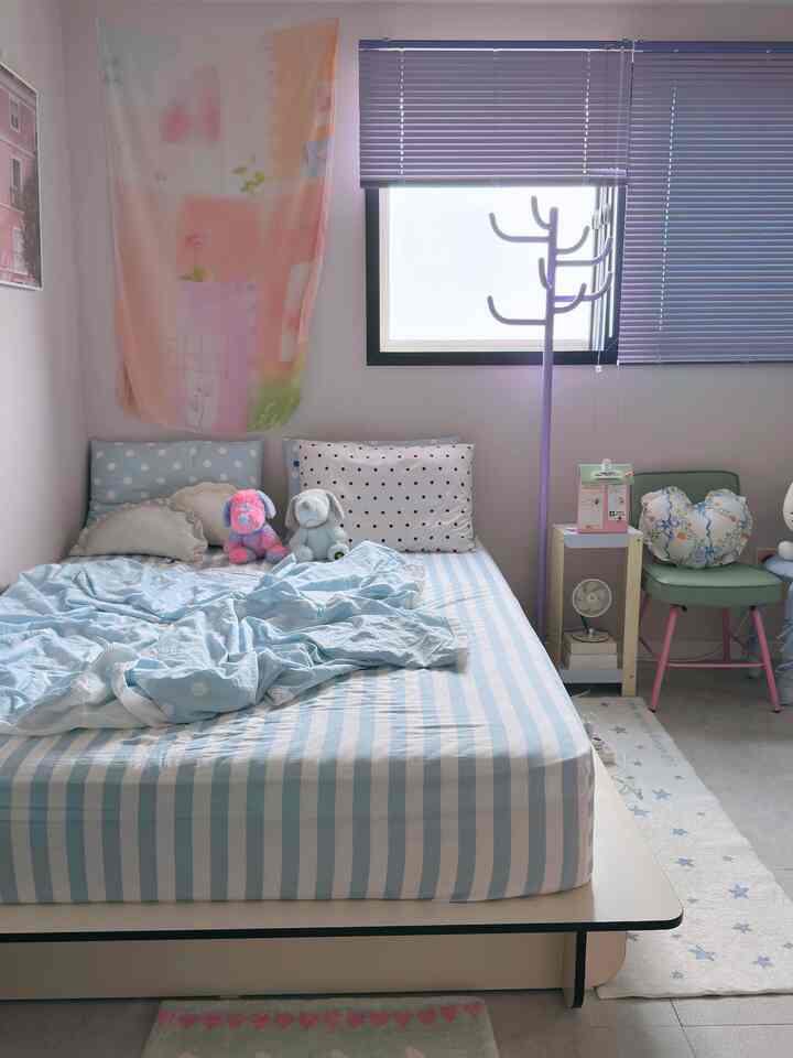 Pastel-toned blinds and striped bedspread in a compact bedroom featuring cute stuffed animals and pink accent decor creating a cozy atmosphere