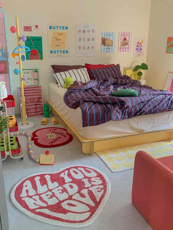 温かみのあるイエローとパステルピンクのトーンのワンルーム寝室、ストライプの寝具とかわいい子供向けのインテリアが配置された雰囲気ある空間