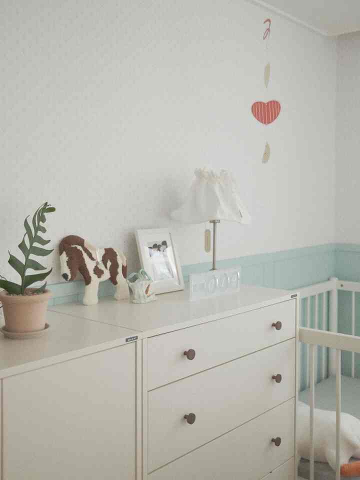 白とミント色調の赤ちゃん部屋、ワードローブとベビーベッドが配置された自然で落ち着いたインテリア