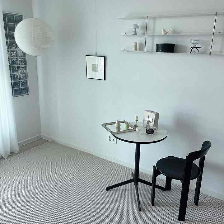 Simple modern single-person living room in white and black tones featuring a small round table and chair in a clean space