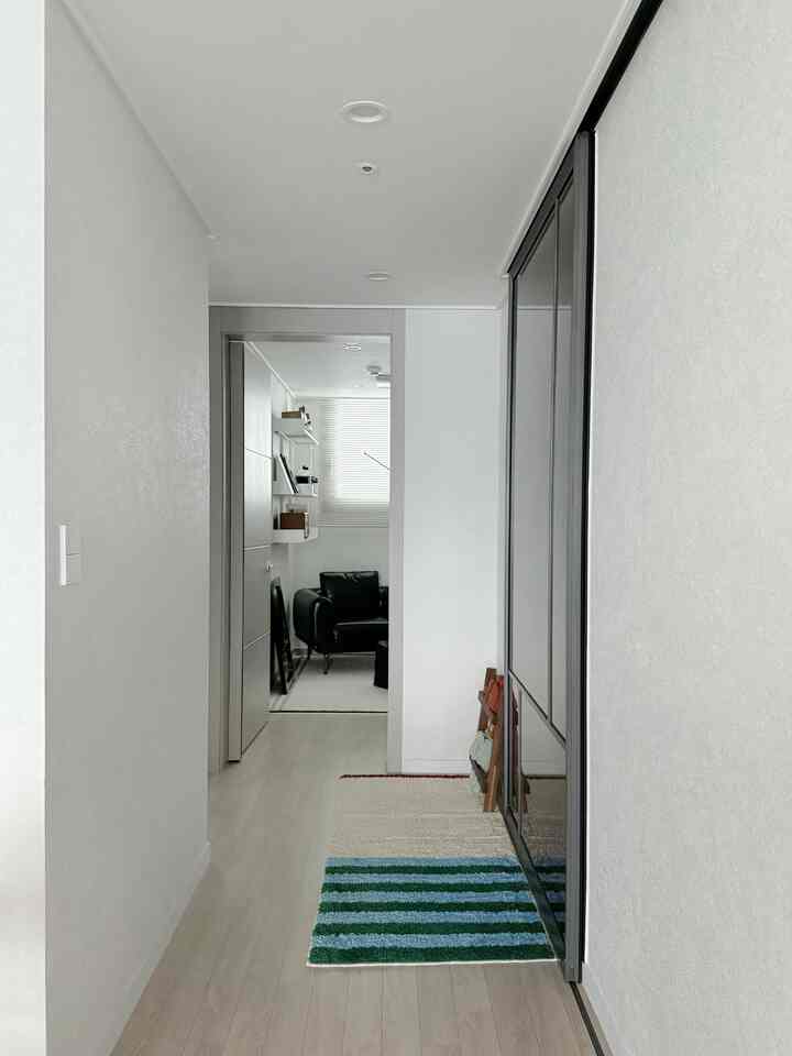 Bright white-toned hallway and modern living room featuring a black sofa and striped rug in a clean space