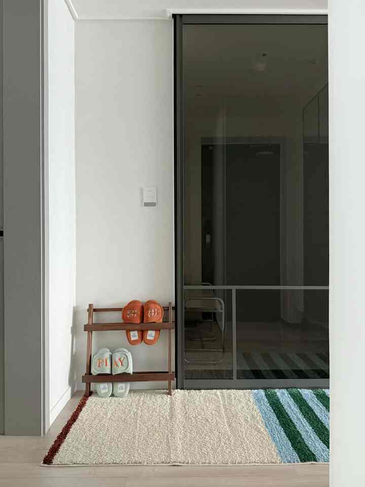 Natural-toned entrance space featuring a wooden slipper rack and beige-green striped rug with minimalist atmosphere