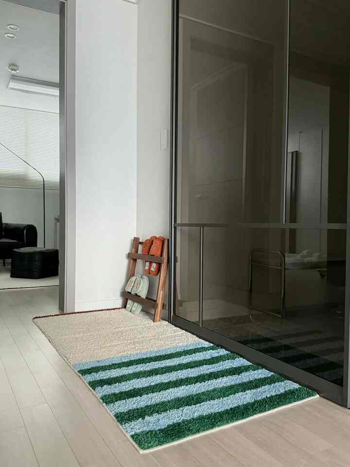 ナチュラルカラーとホワイトの玄関、ストライプラグと木製スリッパラックが配置された明るく清潔感のあるインテリア