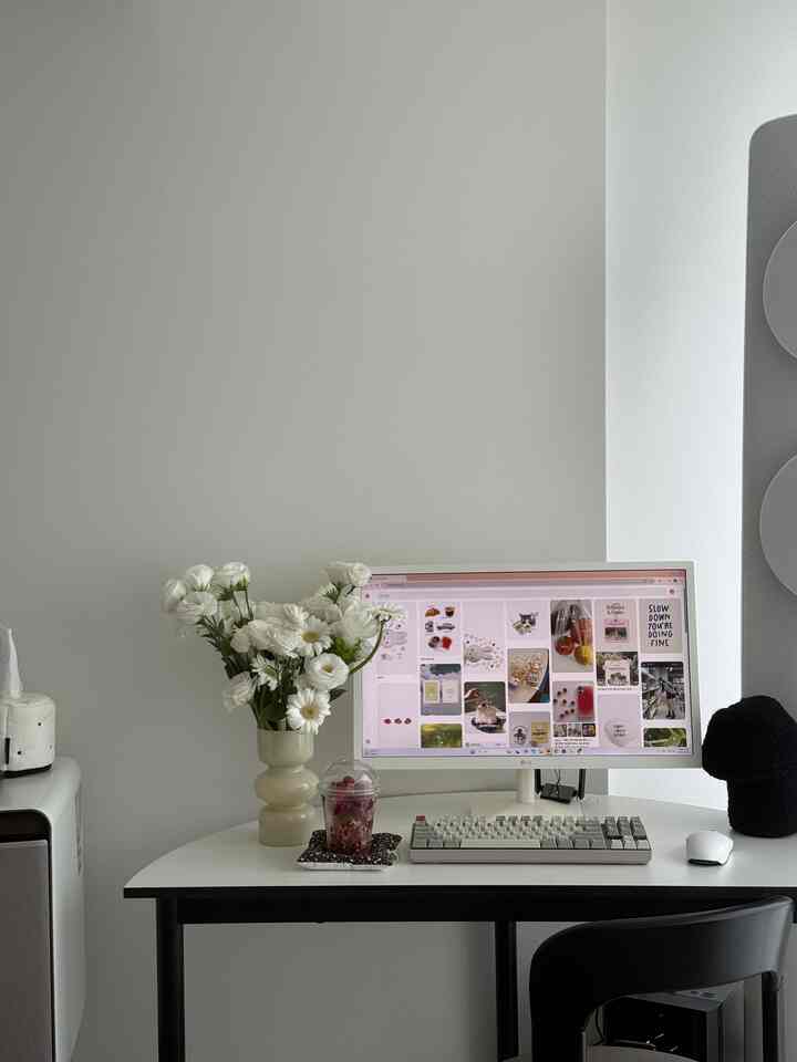 White and black toned home office space with desk featuring monitor, keyboard, and floral vase arranged neatly