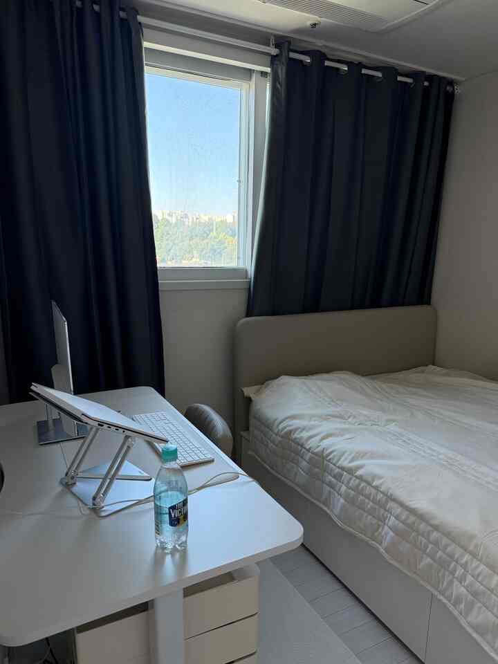 白とグレーのモノトーンの一人用寝室、窓辺にデスクとパソコンが配置された清潔感のあるホームオフィス空間