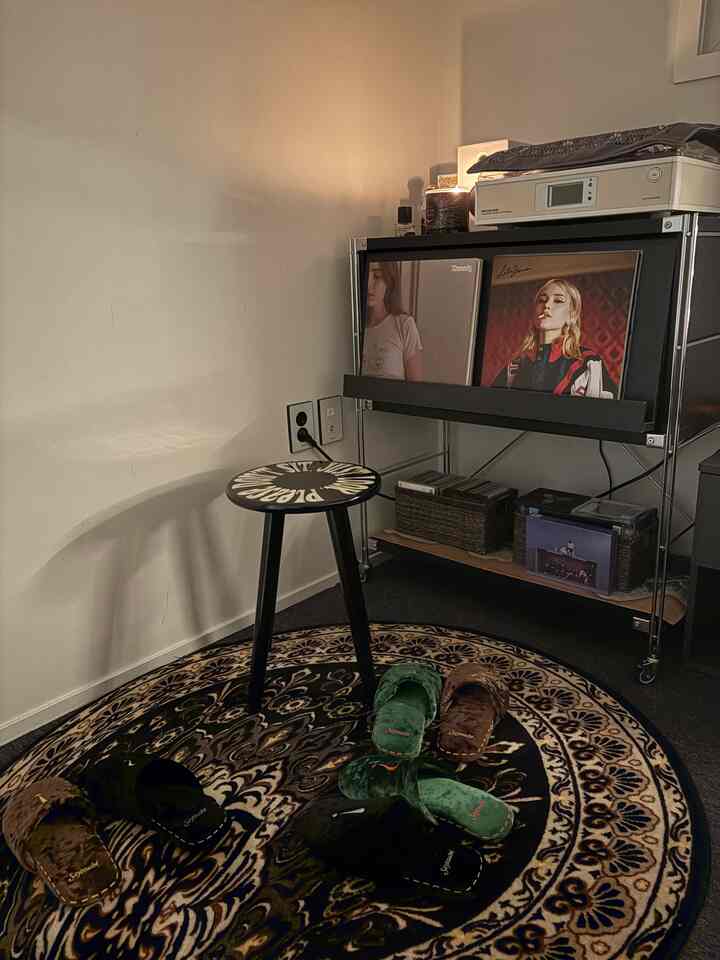 Black and brown toned bedroom corner featuring turntable, rug, and stool with cozy atmosphere