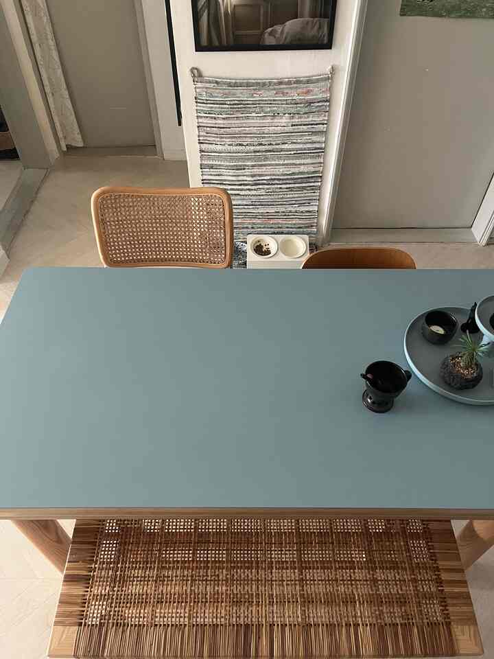 ナチュラルな木目調とブルーのダイニングテーブルが置かれたキッチンの縦長空間、犬用の食器と壁に掛けられたラグが見える雰囲気のあるインテリア