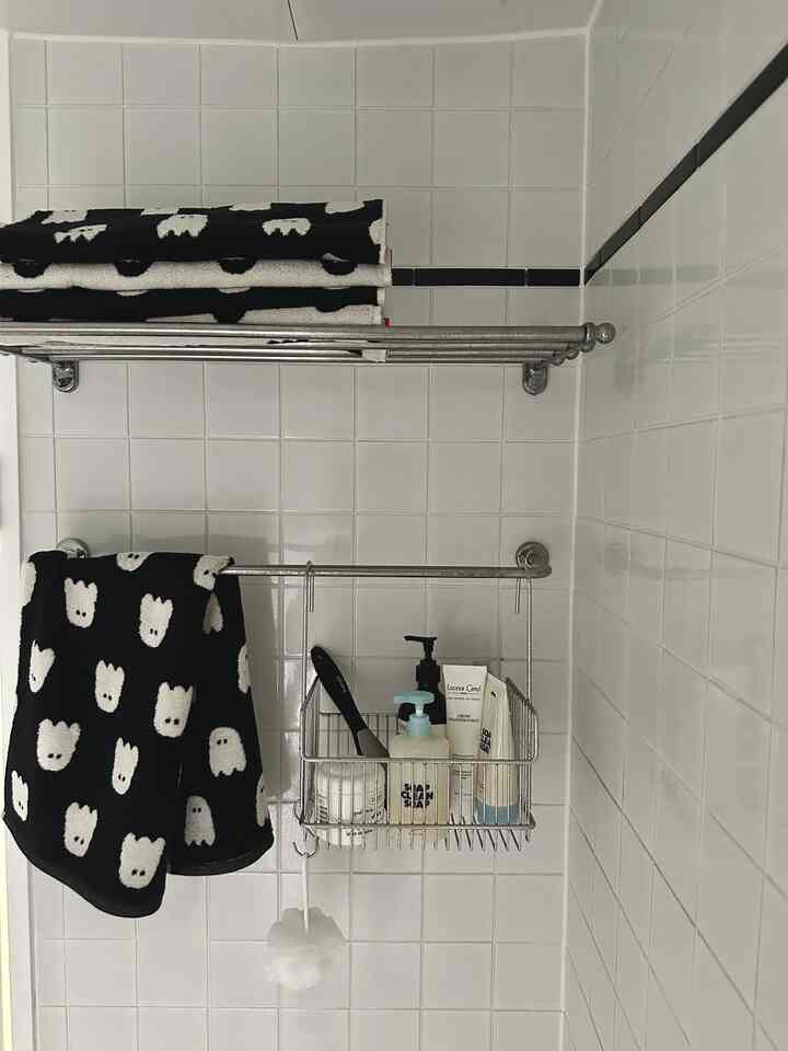 白いタイルのバスルーム、黒いクマの柄のタオルとステンレスのタオル掛け、整頓されたバス用品が配置された清潔感のある空間