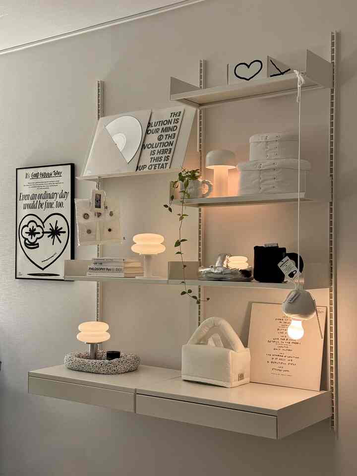 ミルキーなホワイトトーンのモダンな壁棚空間、温かみのある照明と可愛らしいオブジェが配置された居心地の良いインテリア