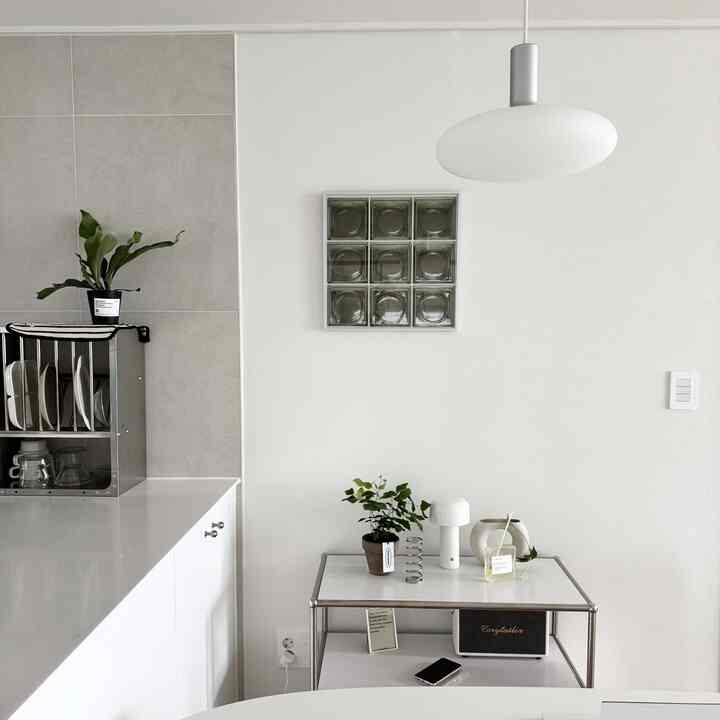 白とグレーのトーンでまとめられたミッドセンチュリーモダンのキッチン、ステンレス製の棚とテーブル、植物が配置されたシンプルなインテリア