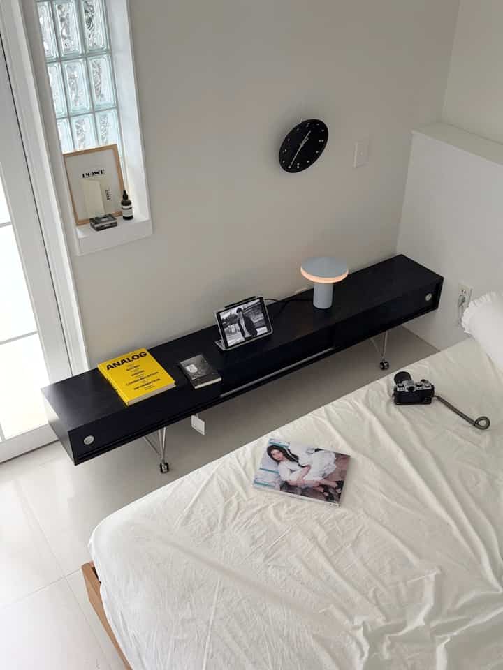 白と黒のトーンでまとめられた寝室、黒いテレビ台とテーブルランプが調和する印象的な空間