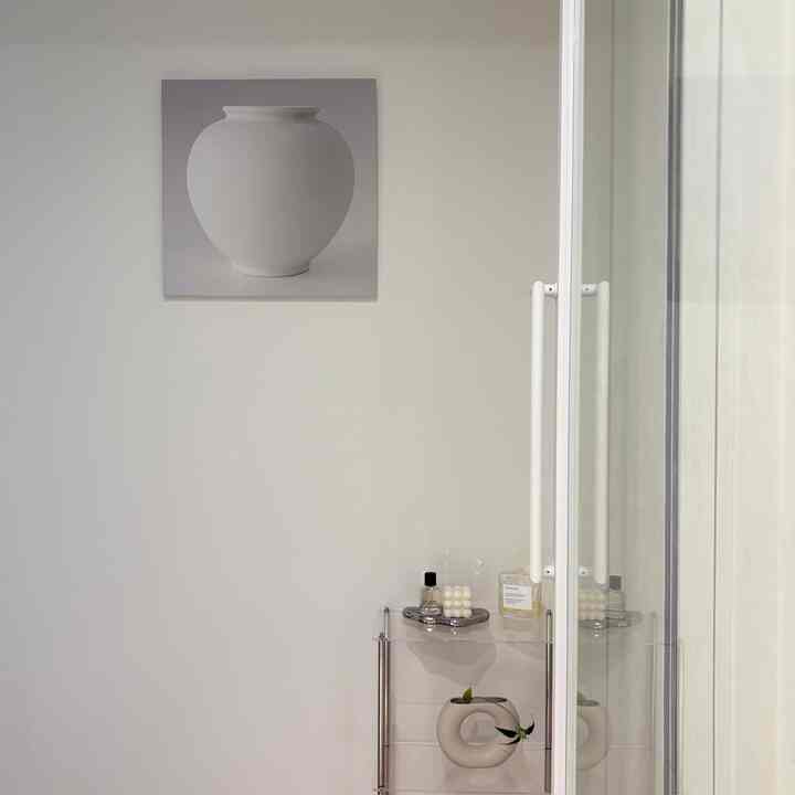 白を基調とした玄関空間、壺の絵額と透明な棚の上にオブジェが配置された、洗練された雰囲気のあるインテリア