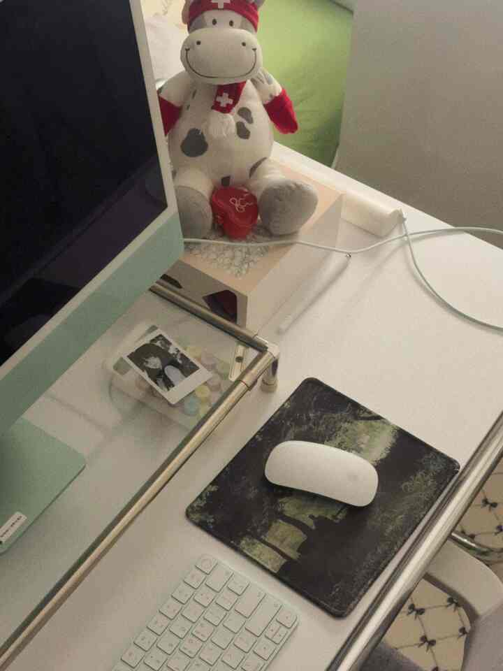 白を基調としたホームオフィス、デスク上にコンピューターモニターとマウスパッド、かわいいぬいぐるみが置かれた雰囲気のある作業スペース