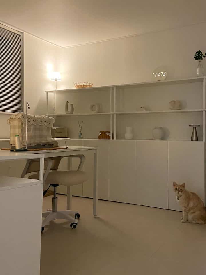 白とナチュラルトーンのリビング、デスクとオフィスチェア、猫がいる雰囲気のある空間