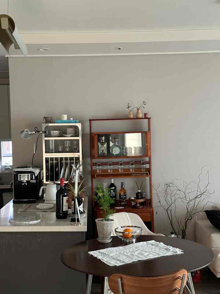 Natural-toned kitchen and dining room space with wooden furniture, wine bottles, and plants arranged in a cozy modern setting