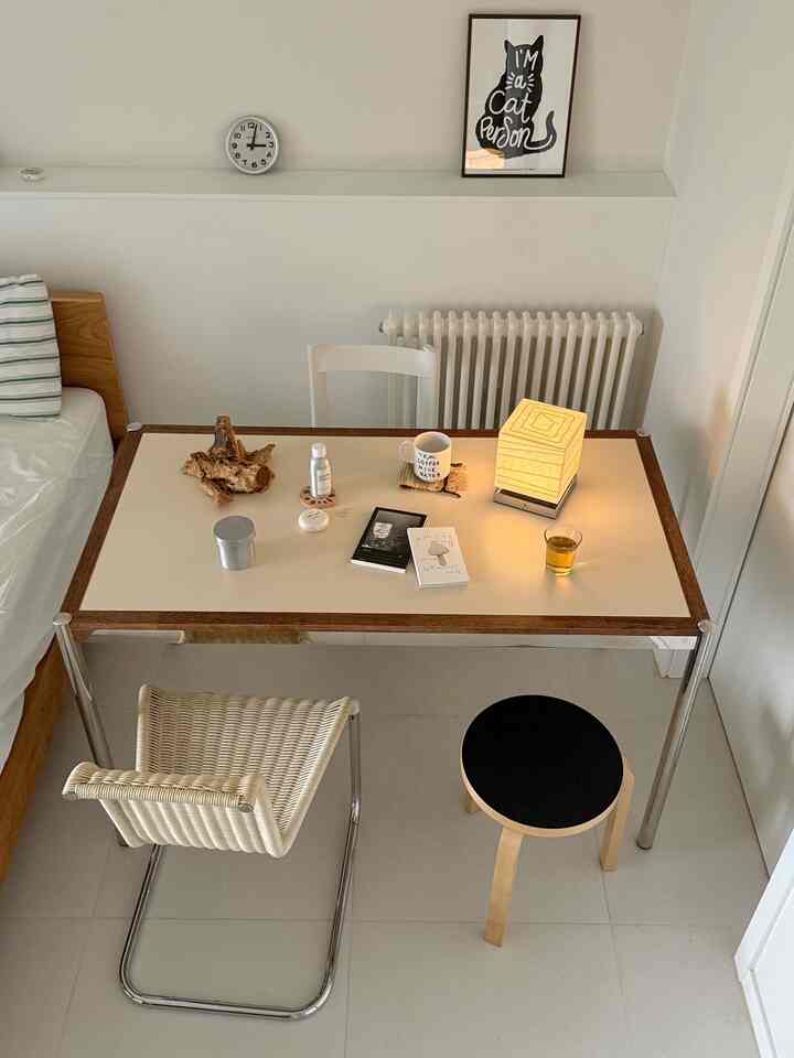 ホワイトとナチュラルトーンの寝室ワークスペース、複数の椅子とテーブルランプが調和したシンプルなインテリア