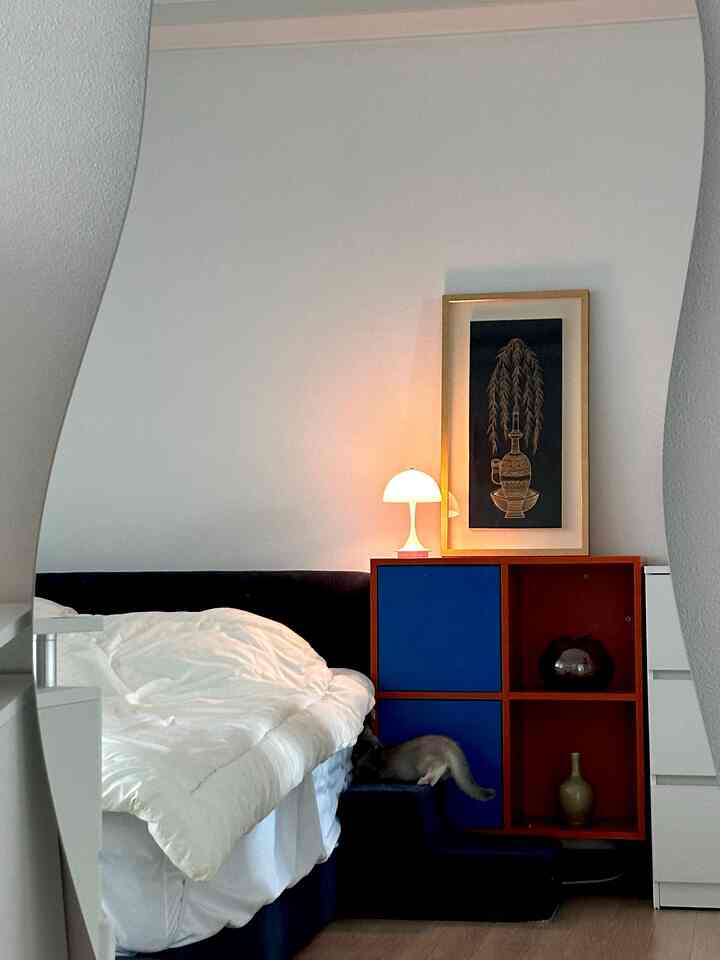 ナチュラルカラーの床とダークブルーのベッドフレームが配置され、サイドテーブルと絵画がある雰囲気のある寝室