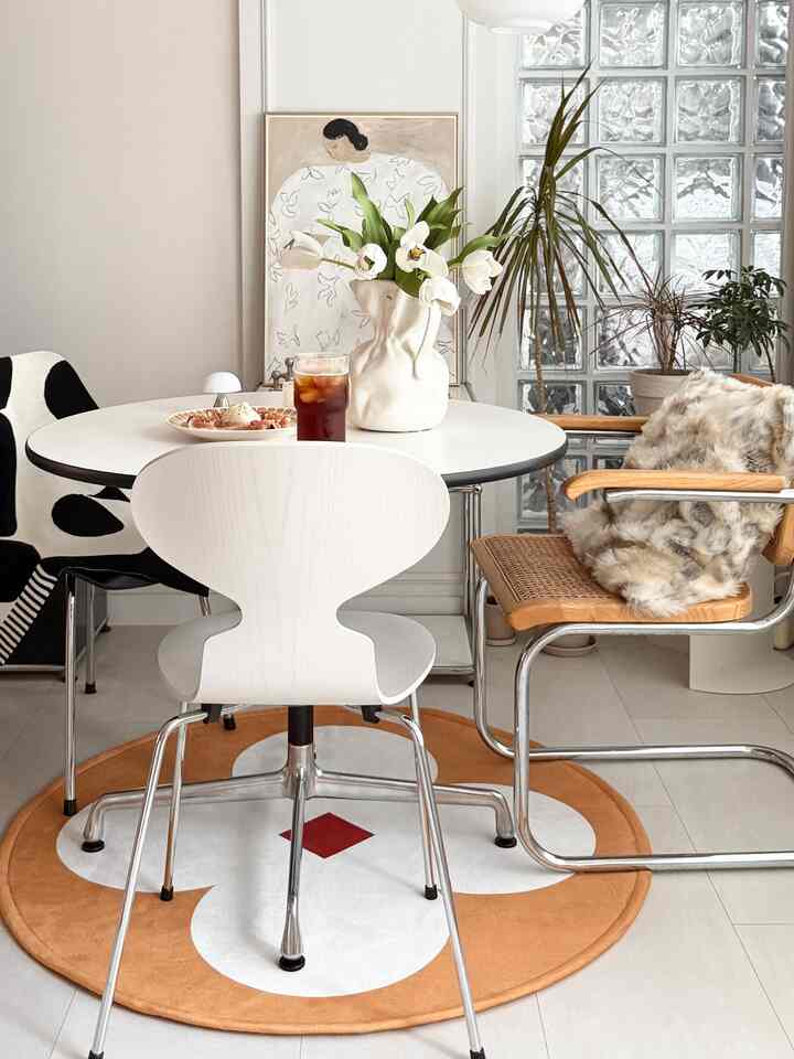 White and natural toned dining room featuring diverse chairs and a vase with tulips in a simple modern space