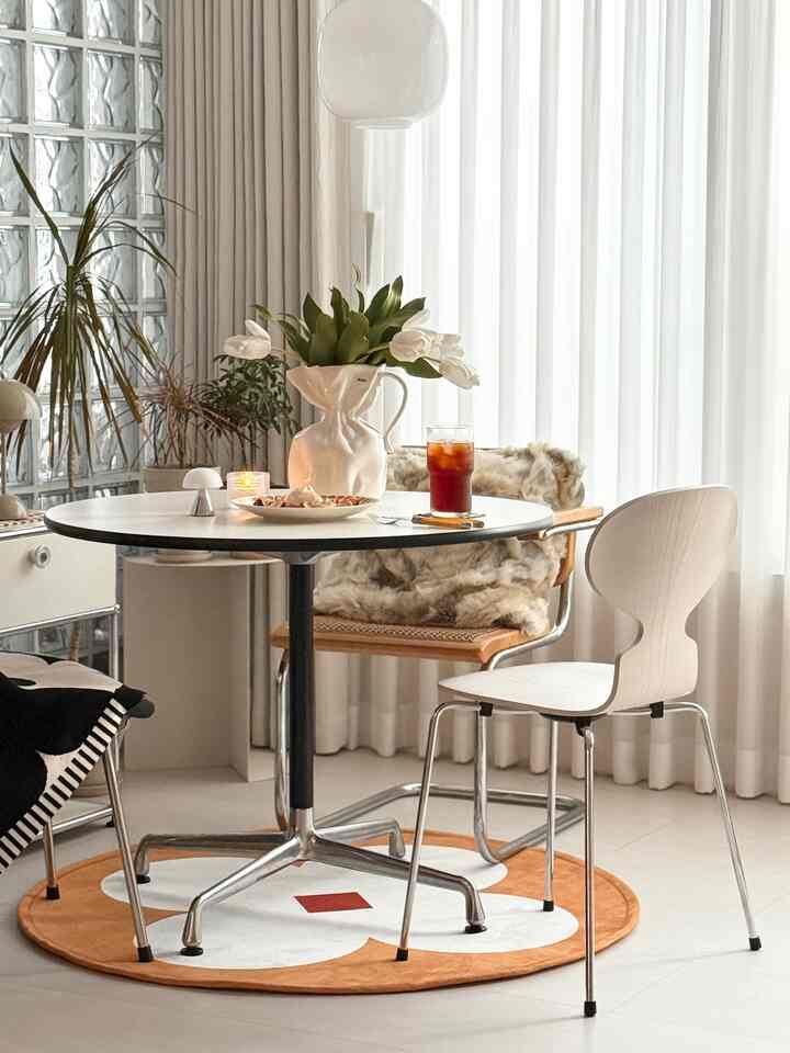 White and beige toned dining room featuring a round dining table, two chairs, curtains, and cozy decor embodying a cafe style atmosphere