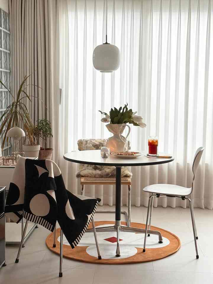 Modern dining room with white curtains backdrop, round dining table and two chairs, complemented by an orange rug