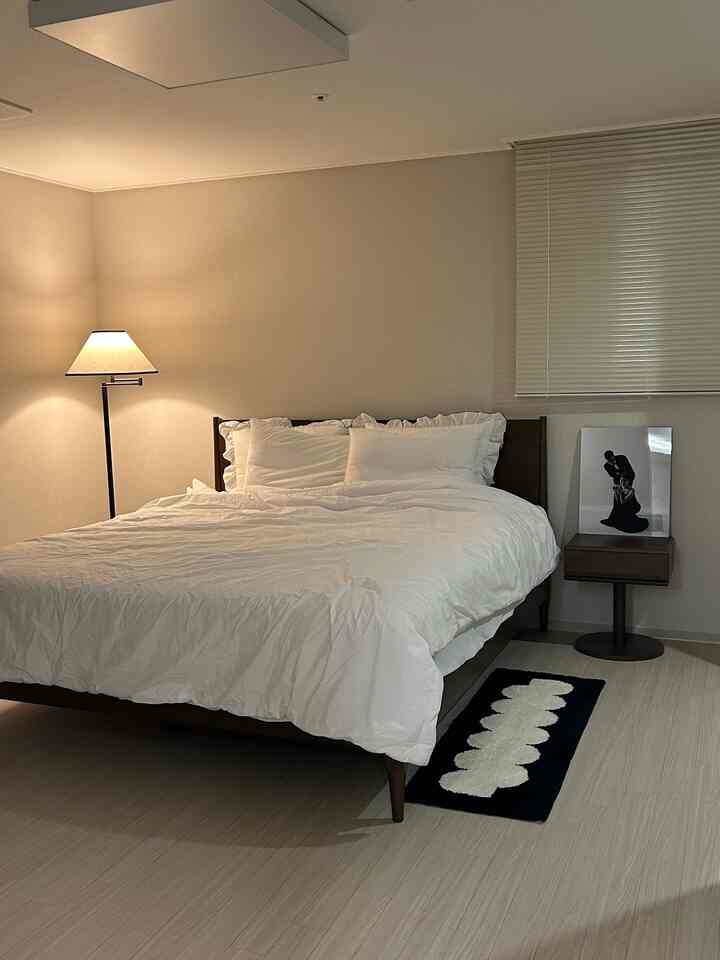 白と茶色のトーンでまとめられたシンプルでモダンな寝室、ベッド、フロアランプ、ナイトテーブルが配置された印象的な空間