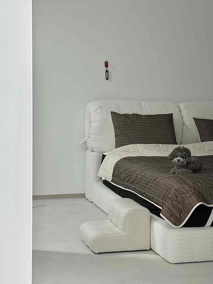 A cozy bedroom in ivory and brown tones featuring a plush bed frame and pet steps, with a small dog resting comfortably on the blanket
