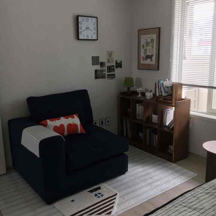 ネイビーのアームチェアと木製の本棚が配置されたナチュラルモダンなリビング、白い壁とブラインドの窓が特徴的な空間