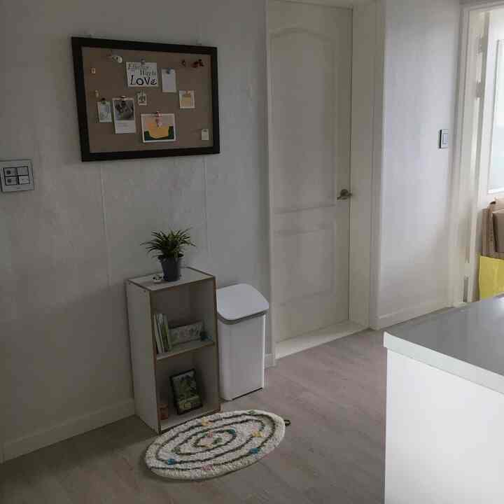 白とナチュラルカラーの小さな部屋、コンパクトな収納棚と植物が配置された清潔感のある玄関スペース