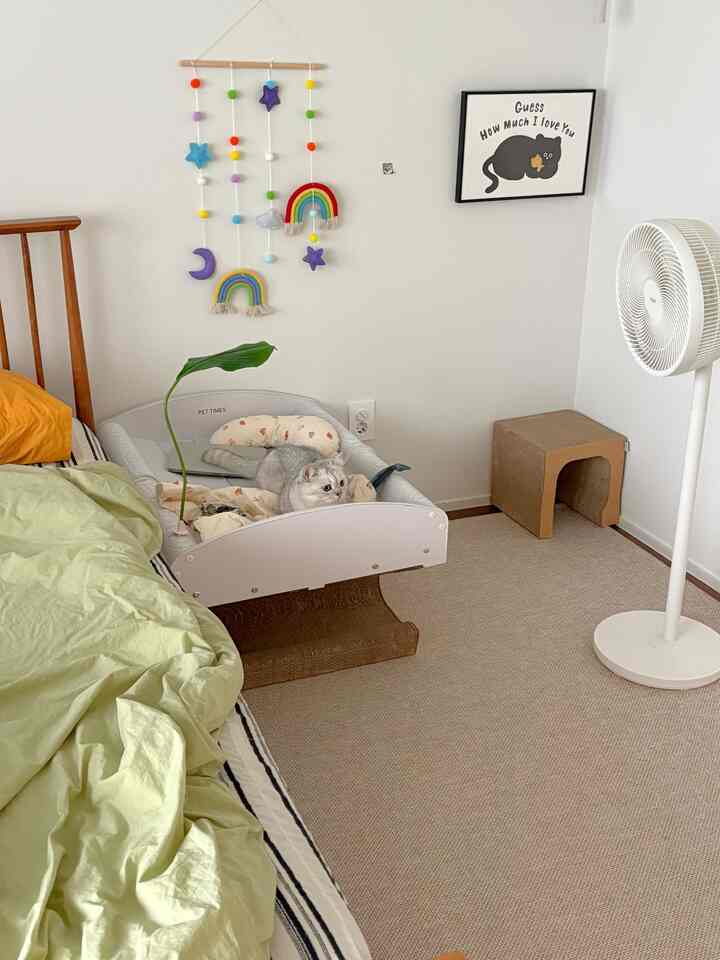 白とベージュの色調の寝室、猫用ベッドとカラフルなモビールが配された雰囲気のあるインテリア