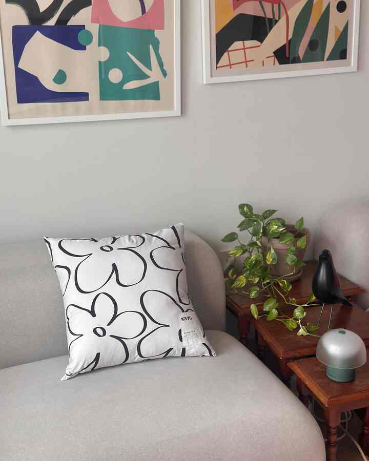 明るいグレーのソファに白い花柄クッション、ブラウンのサイドテーブルと緑の植物が配置されたナチュラルモダンなリビング