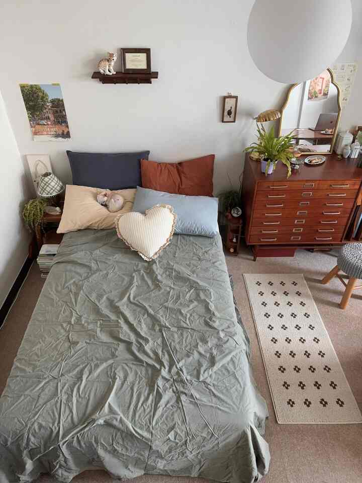 ウッドトーン家具とナチュラルグリーンの寝具が印象的な小さな寝室、ベッドに小型犬が休む落ち着いた空間