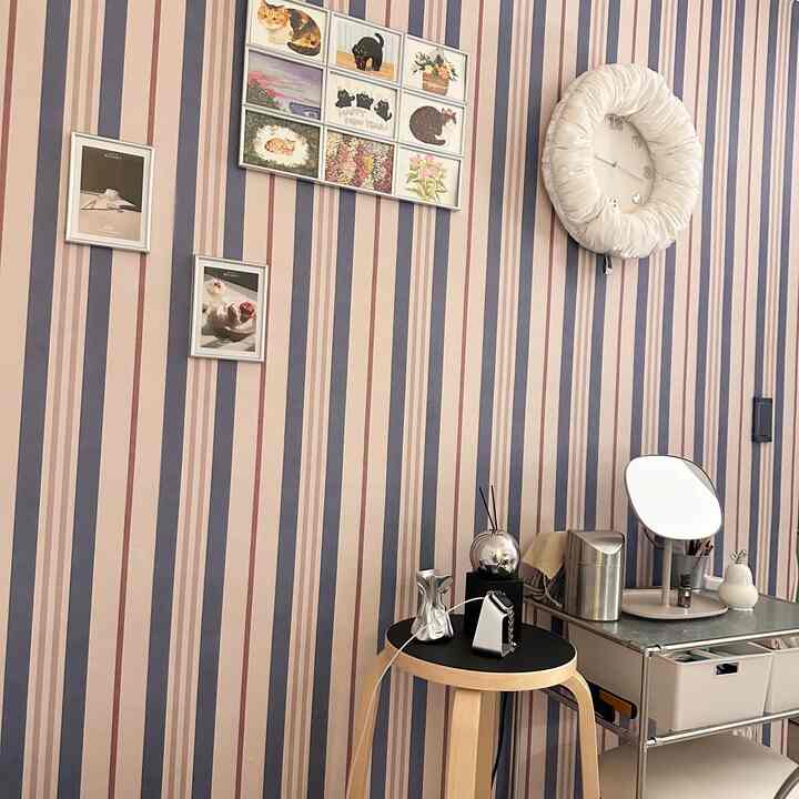 ピンクとネイビーのストライプの壁にバースツール、小さな鏡、壁時計、額入りの絵が配置されたナチュラルな印象のリビング空間