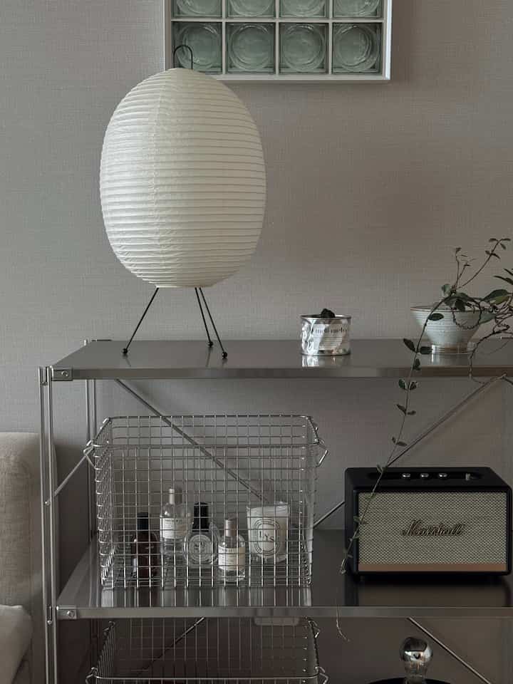 グレーの壁とシルバーのステンレス製棚、白い和紙のランプと多様な装飾品が配されたモダンなリビングスペース