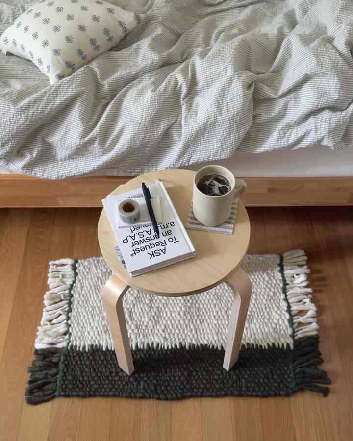 ナチュラルカラーと木目調が調和する4.5畳の寝室、小さな丸い木製スツールと快適な寝具が配置されたミニマルな空間