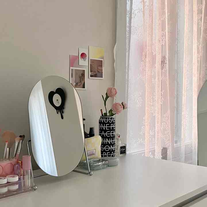 Cozy vanity space with white and pink lace curtains and an oval tabletop mirror creating a soft atmosphere