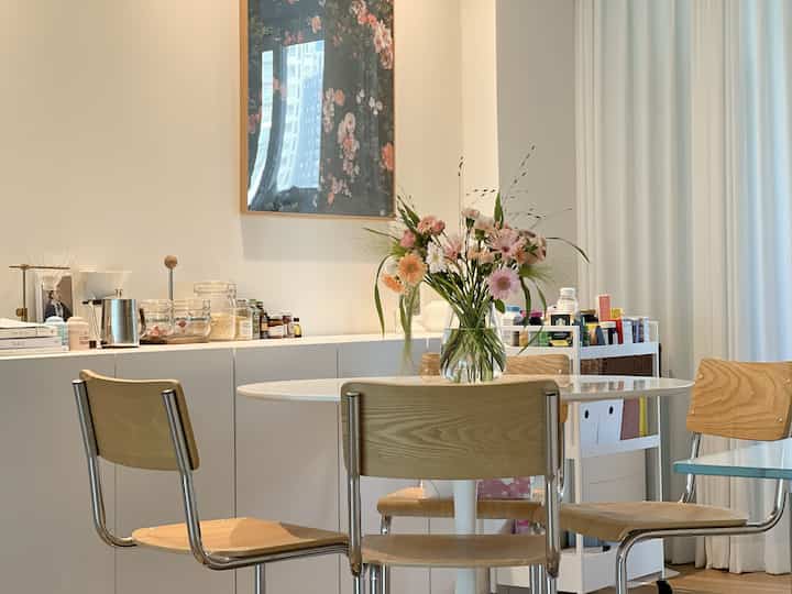 白と木目調の調和した4人用ダイニング、中央に花瓶が置かれたテーブルと椅子が配置されたナチュラルな空間