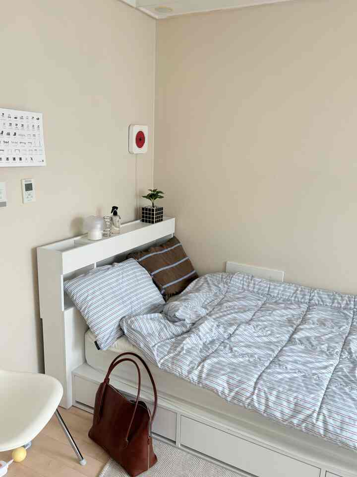 ベージュの壁とブルー・ブラウンの寝具が配置されたワンルームの寝室、自然で落ち着いた雰囲気のあるインテリア