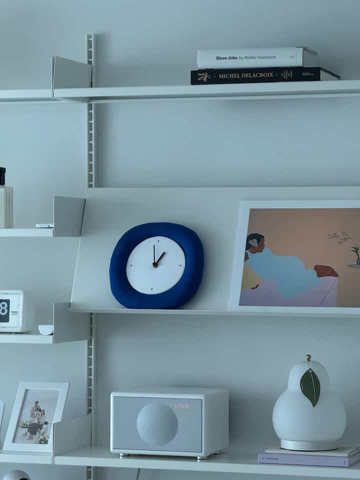 白い壁と棚にブルーのファブリック製モダン壁時計と装飾品が配置された、モダンでシンプルなインテリア