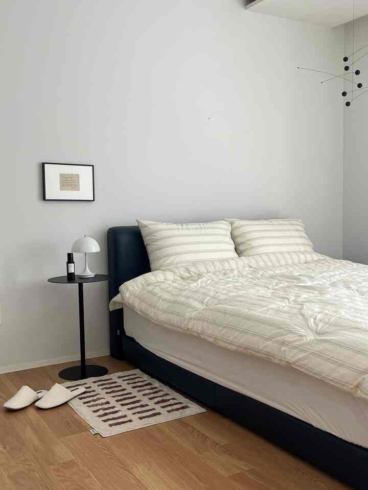 Modern bedroom with white walls, natural wood flooring, black bed frame and side table, featuring warm bedding textiles