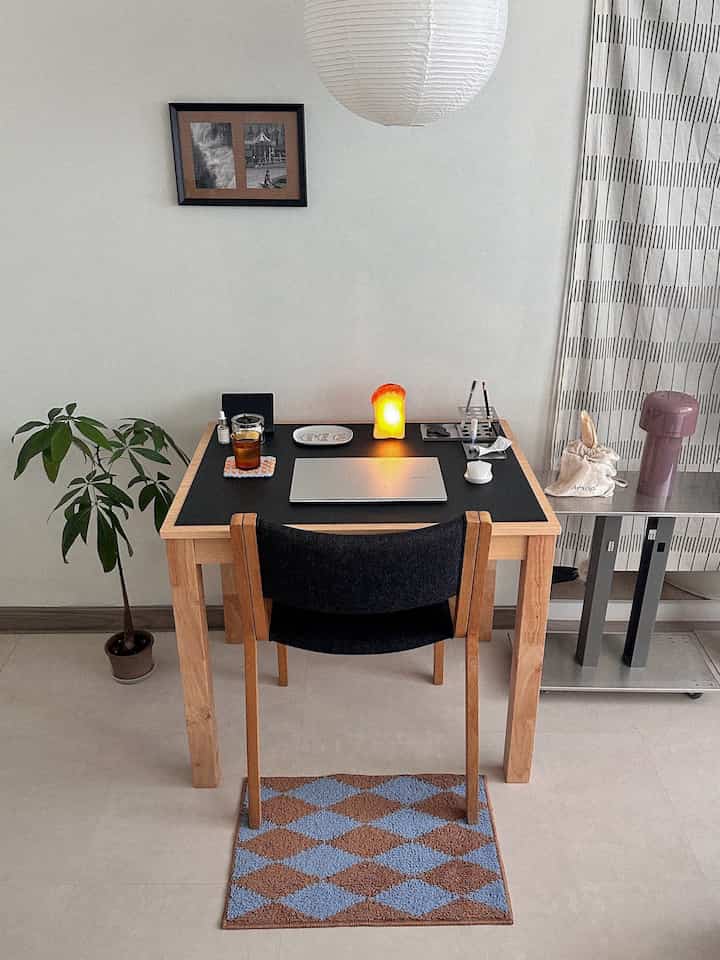 ウッドトーンとブラックのワンルームのホームオフィス、デスクと椅子、植物、テーブルランプが配置された雰囲気のあるシンプルなインテリア