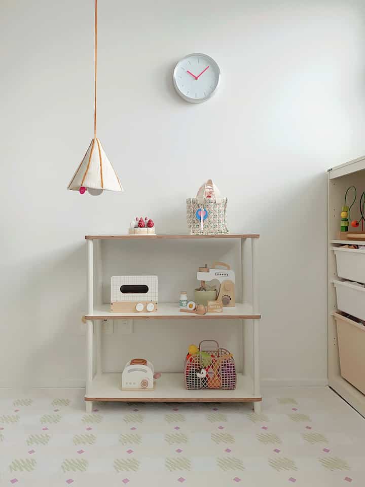 白とベージュの色調の子供部屋、棚とおもちゃ、時計が配された清潔感のあるインテリア