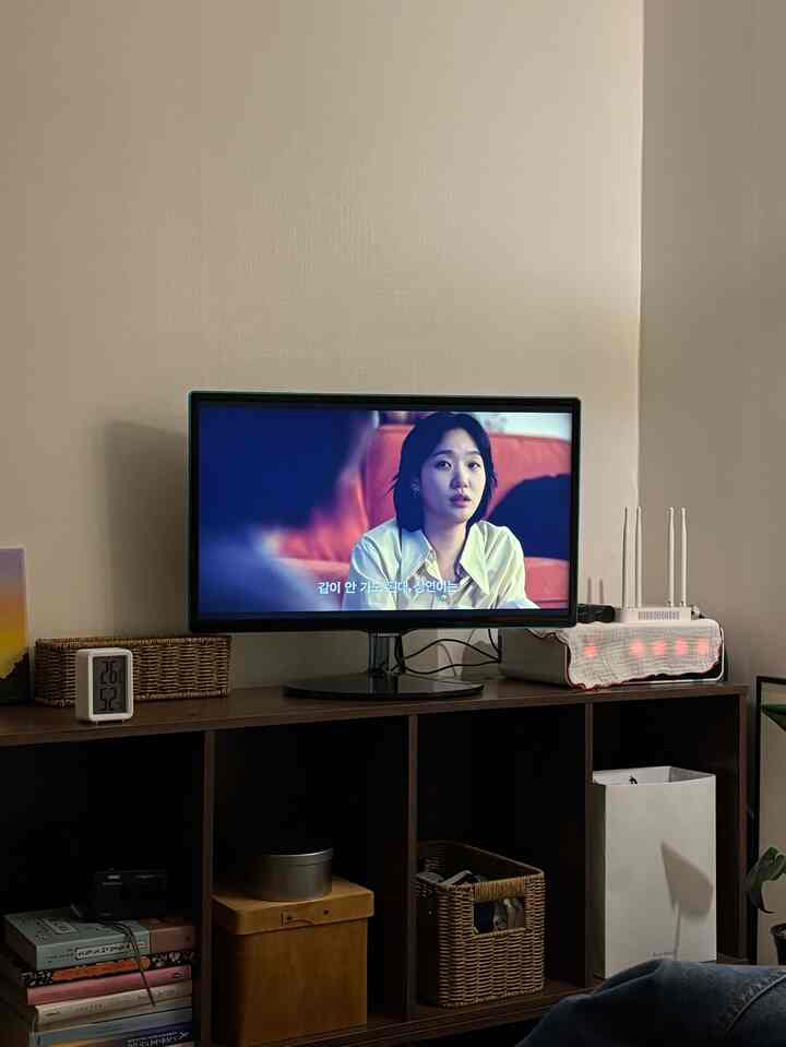 明るい壁とブラウンのナチュラル家具が配置されたリビング、テレビ台の上にサムスンのモニターが置かれたシンプルで自然なインテリア